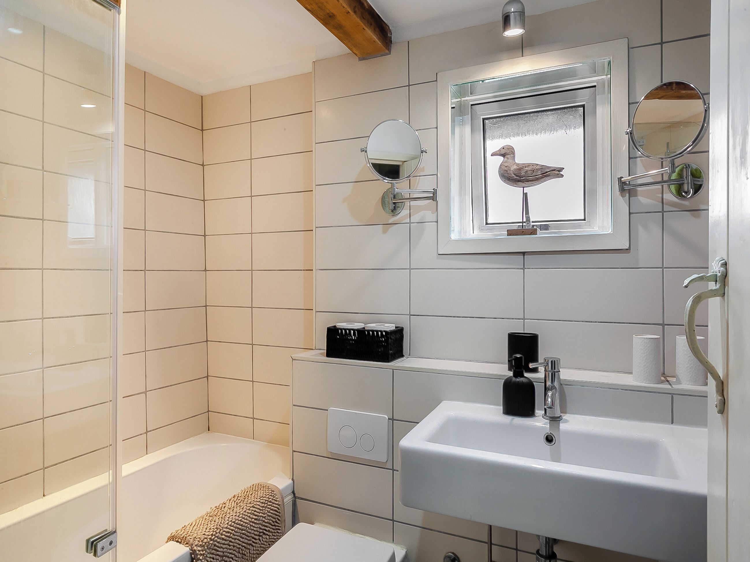A bathroom with a bathtub, a sink, a mirror, and a framed picture of a bird.