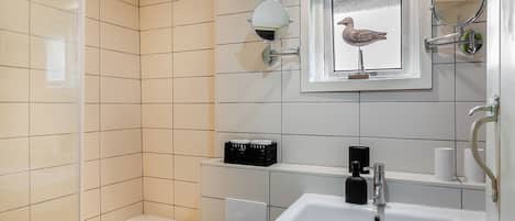A bathroom with a bathtub, a sink, a mirror, and a framed picture of a bird.