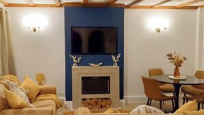 A living room with a fireplace, sofas, a dining table, and a TV mounted on the wall.