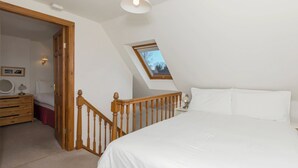 A bedroom with a large bed, a wooden staircase, a skylight, and a nightstand with a lamp.