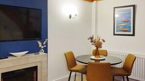 A dining area with a round table, four chairs, a vase with flowers, a flat-screen TV mounted on the wall, and a framed picture above the table.