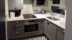 A modern kitchen with grey cabinets, a microwave, a kettle, and a sink.