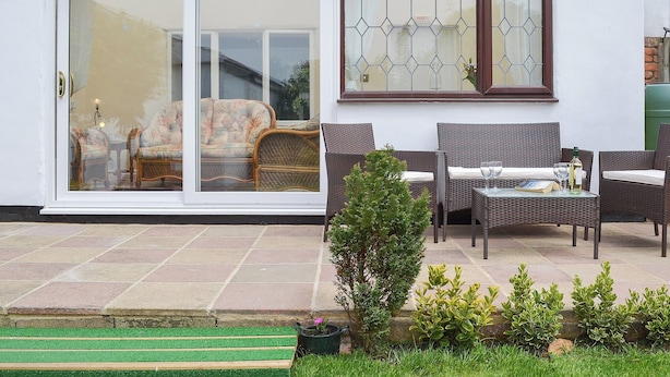 A patio area with wicker furniture, a glass door leading to a room, and a small garden with a bench and plants. - 2 bedroom accommodation in Buckton, near Bridlington (Buckton, near Bridlington)