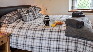A bed with a plaid bedspread, a bedside table with a lamp, and a window with curtains. - 2 bedroom accommodation in Buckton, near Bridlington (Buckton, near Bridlington)