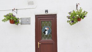 A brown door with a glass panel, a sign reading "11A PUPIN COTTAGE", and two hanging flower pots with purple flowers. - 2 bedroom accommodation in Buckton, near Bridlington (Buckton, near Bridlington)