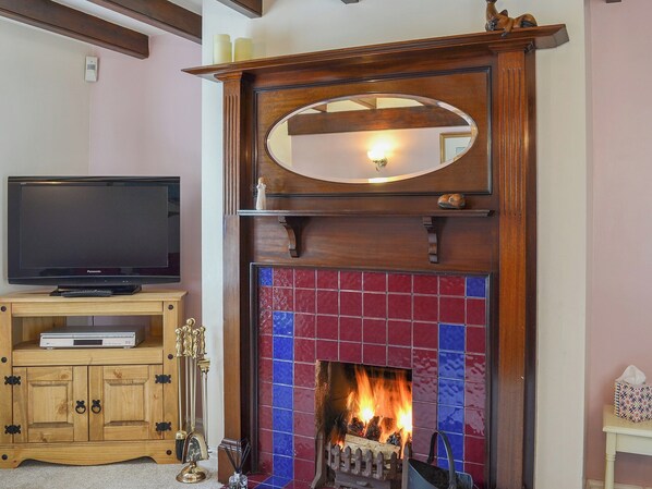 A living room with a television on a wooden cabinet, a fireplace with a tiled surround, and a mirror above the mantel.