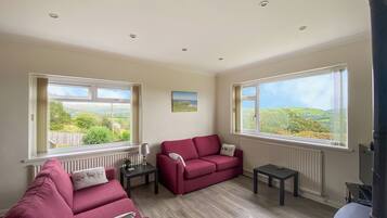 A room with two red sofas, a small table, and two windows with views of greenery.