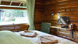 Ein Zimmer in einer Holzhütte mit einem Bett, einem Tisch, einem Stuhl und einem Fenster mit Vorhängen.