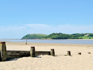Une plage de sable avec des poteaux en bois et un panneau vert, indiquant le chemin vers une colline sur laquelle se dresse une structure ressemblant à un château.