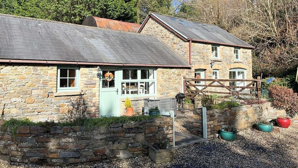 A stone building with a green door, a sign reading 'BEURY,' and a garden with potted plants. - 2 bedroom accommodation in Llannon, Llanelli (Llannon, Llanelli)