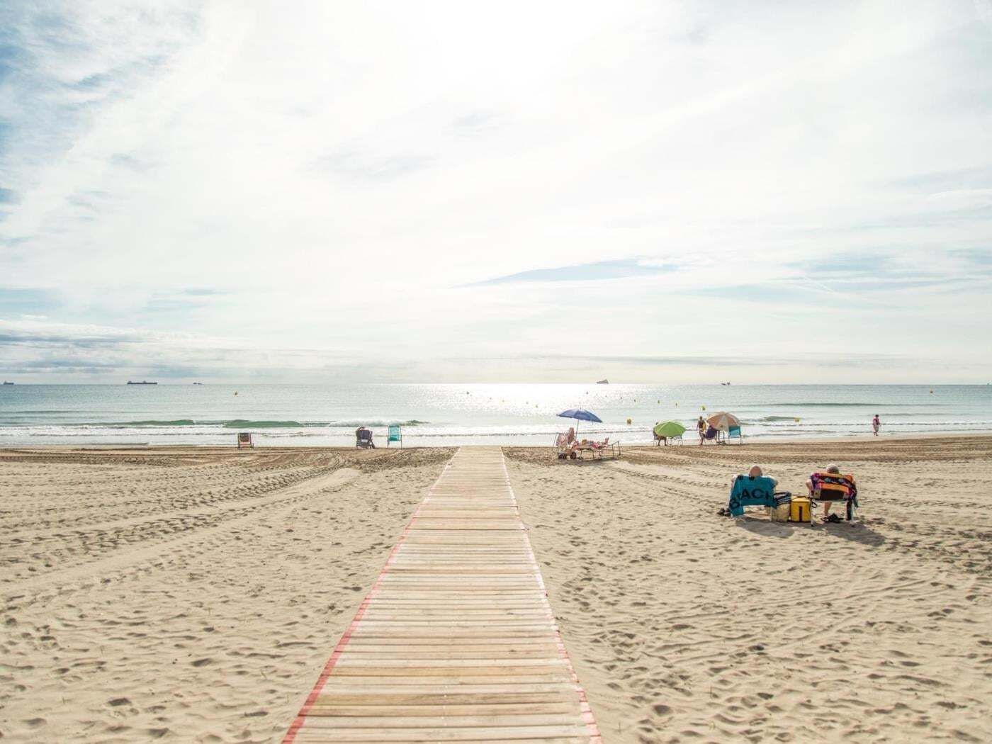 A beach with a wooden boardwalk leading to the water, umbrellas, and beach chairs.