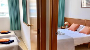 A hotel room with a bed, a bedside table with a lamp, a chair, and a window with curtains. - APARTBEACH VANCOUVER RELAX CLIMATIZED AND PARKING (SALOU)