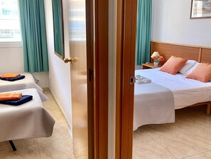 A hotel room with a bed, a bedside table with a lamp, a chair, and a window with curtains.