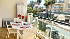 A balcony with a dining table set for four, white chairs, a white cabinet, and a view of a street with palm trees and buildings. - APARTBEACH VANCOUVER RELAX CLIMATIZED AND PARKING (SALOU)