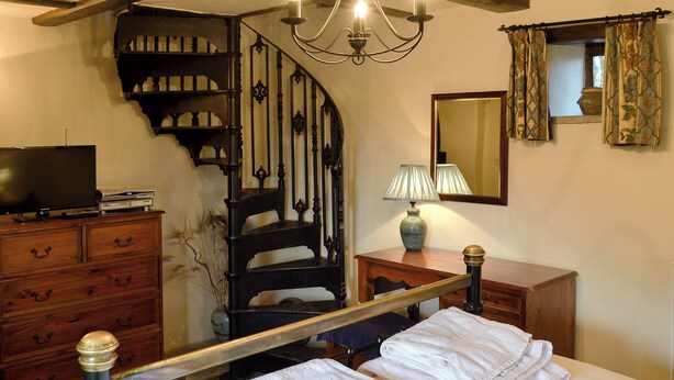 A bedroom with a bed, a wooden dresser, a mirror, a lamp, and a staircase. - 1 bedroom accommodation in Castleton (Castleton)
