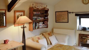 A cozy living room with a sofa, a coffee table, a lamp, a bookshelf, and a clock on the wall. - 1 bedroom accommodation in Castleton (Castleton)