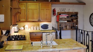 A kitchen with wooden cabinets, a microwave, a sink, and a gas stove. - 1 bedroom accommodation in Castleton (Castleton)