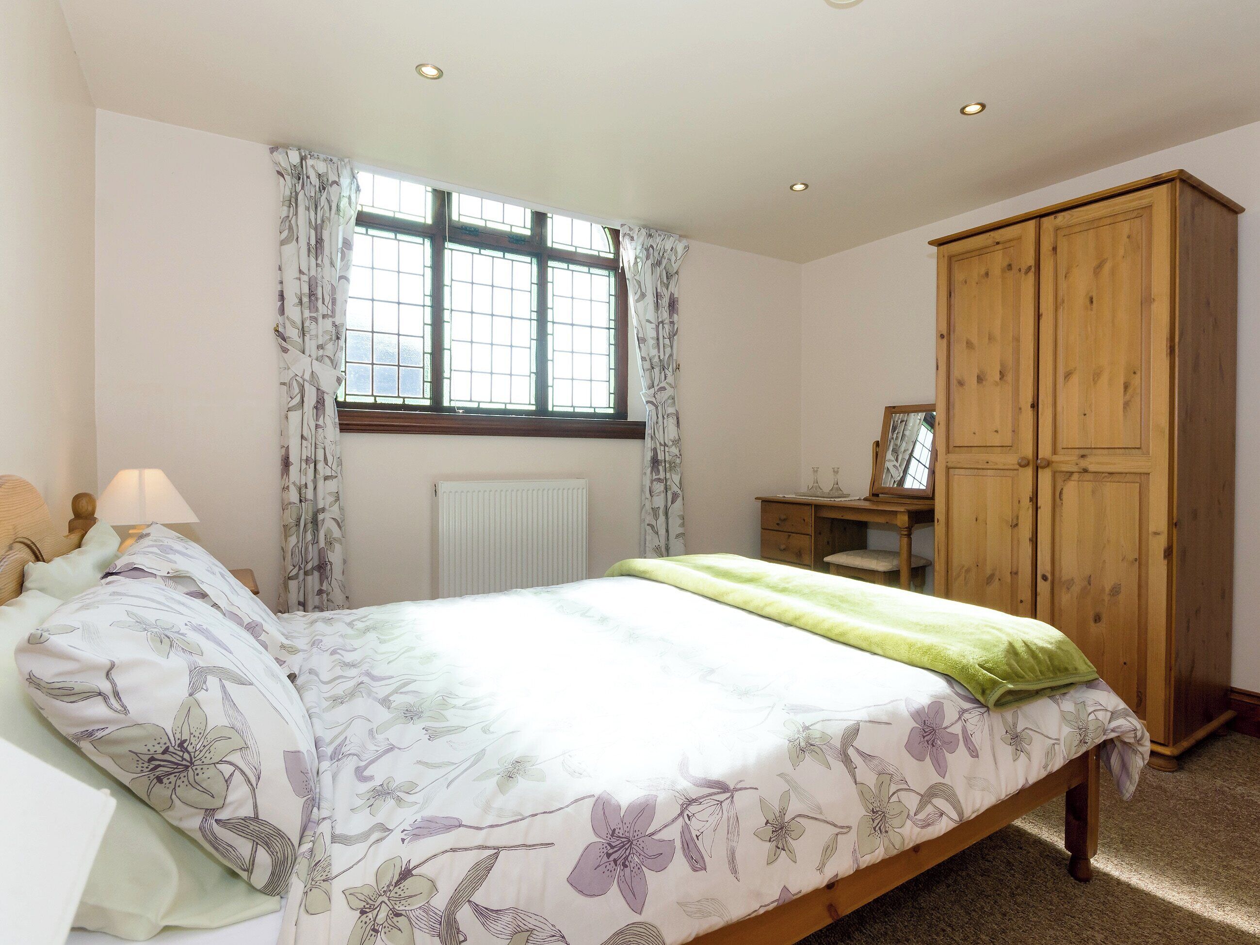 A bedroom with a bed, a dresser, a mirror, and a window with curtains.