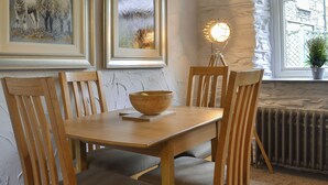 A dining area with a wooden table, chairs, a bowl, framed artwork, a lamp, and a window with a view. - Coach House Grasmere (Grasmere)