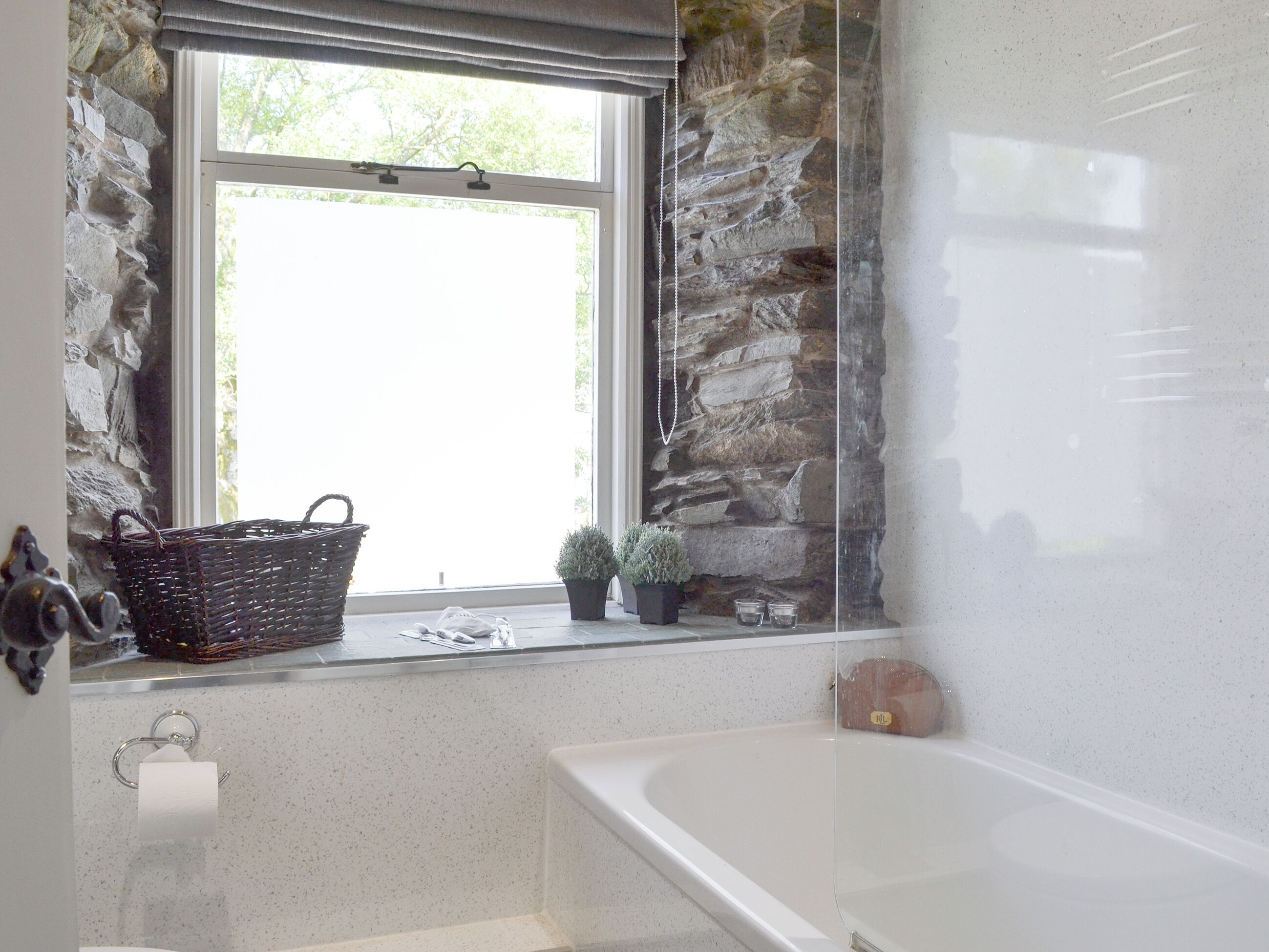 A bathroom with a bathtub, a window with a stone wall, a basket, and a potted plant.