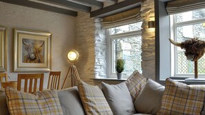 A cozy living room with a sectional sofa, a tripod floor lamp, a framed artwork, and a stone wall. - Coach House Grasmere (Grasmere)