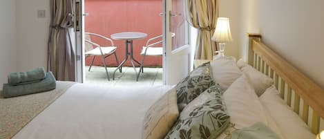 A hotel room with a bed, a small table with chairs, a balcony with a view, and a lamp.