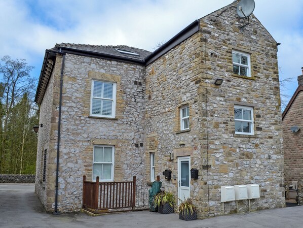 A stone building with multiple windows, a door, and a small fenced area with potted plants.
