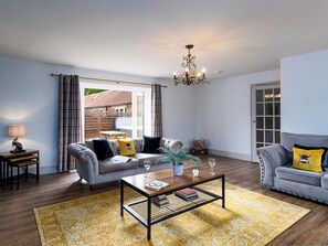 A living room with a grey sofa, a coffee table, a yellow rug, and a chandelier.