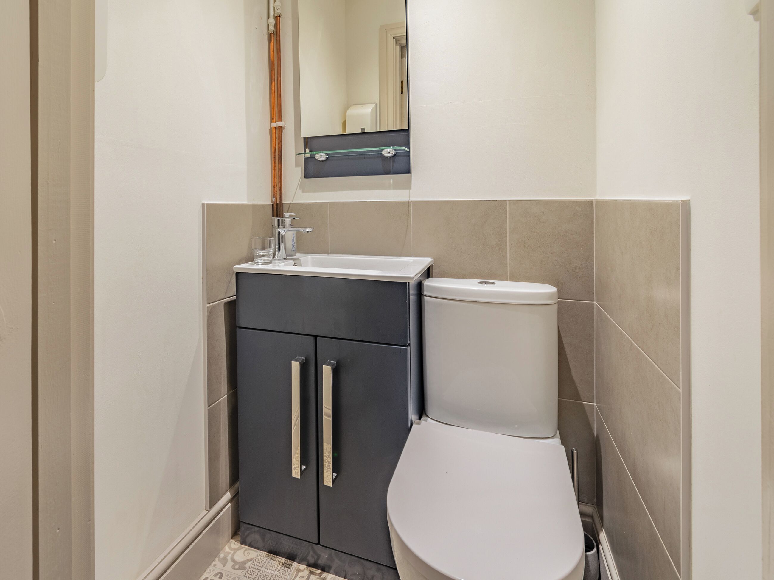 A bathroom with a white toilet, a dark cabinet with two drawers, and a mirror above the sink.