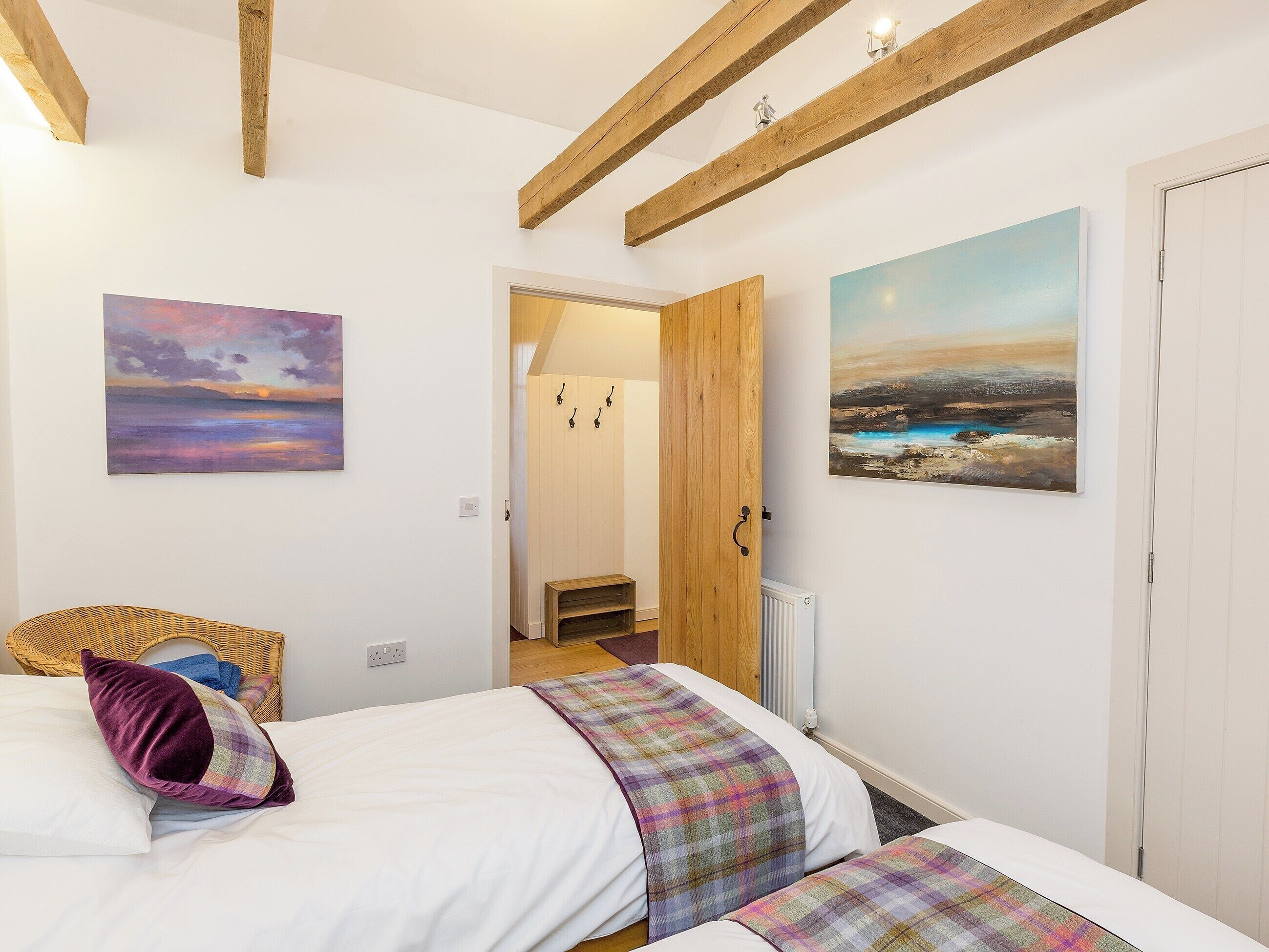 A bedroom with a bed, a wooden door, and two paintings on the wall.
