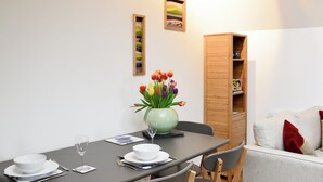 Un coin repas avec une table dressée pour deux personnes, un vase de tulipes et un buffet en bois adossé au mur.