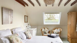 A bedroom with a large bed, two wicker chairs, a wooden cabinet, and a window with a view of trees. - 3 bedroom accommodation in Fitzhead, near Wivelscombe (Fitzhead, near Wivelscombe)