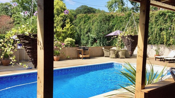 A rectangular swimming pool with a wooden deck surrounding it. - 3 bedroom accommodation in Fitzhead, near Wivelscombe (Fitzhead, near Wivelscombe)