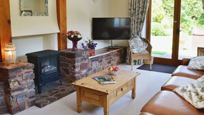 A cozy living room with a stone fireplace, a television, a wicker chair, and a sofa. - 3 bedroom accommodation in Fitzhead, near Wivelscombe (Fitzhead, near Wivelscombe)