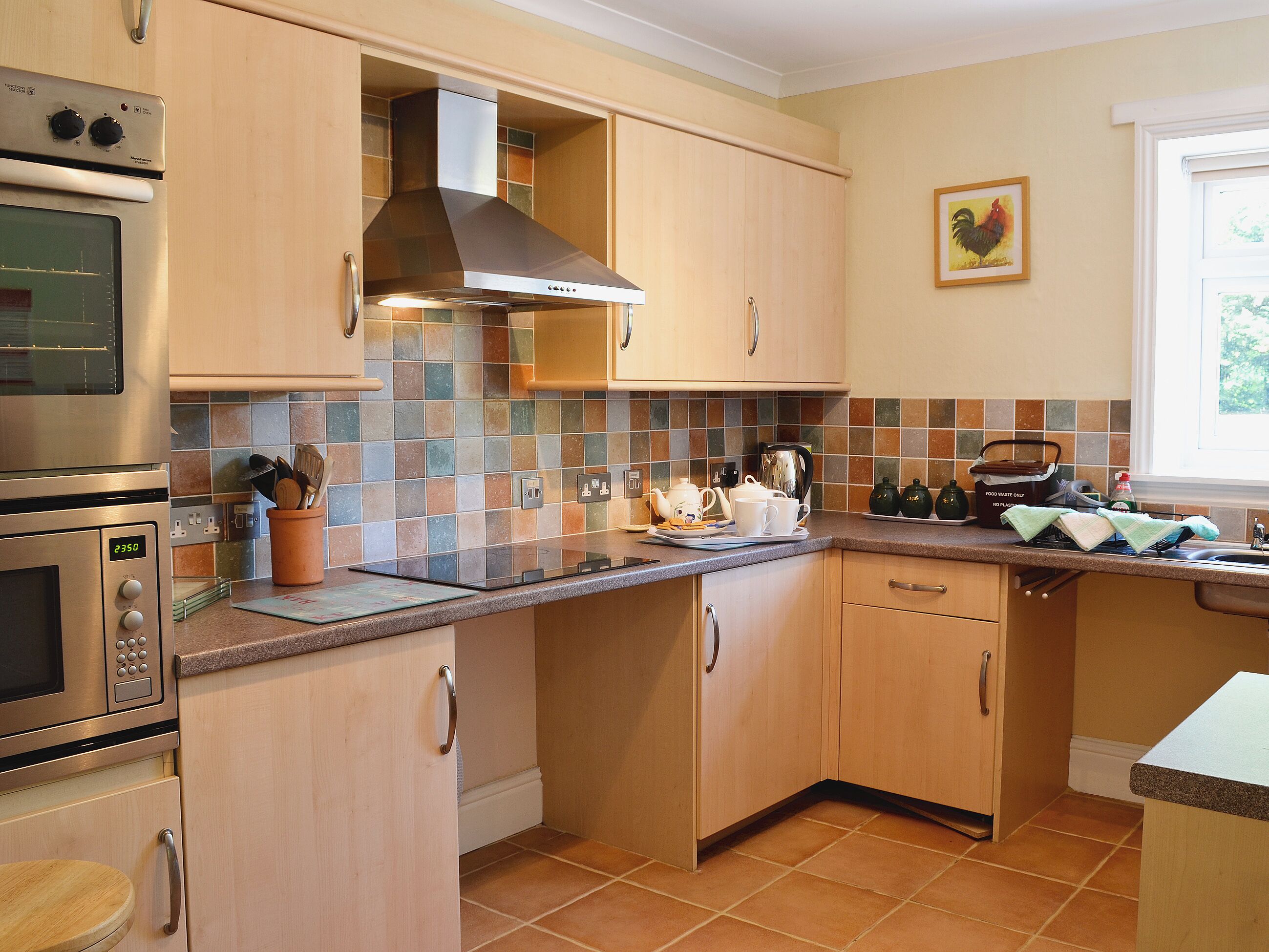 Een keuken met houten kastjes, een roestvrijstalen fornuis en een betegelde achterwand.