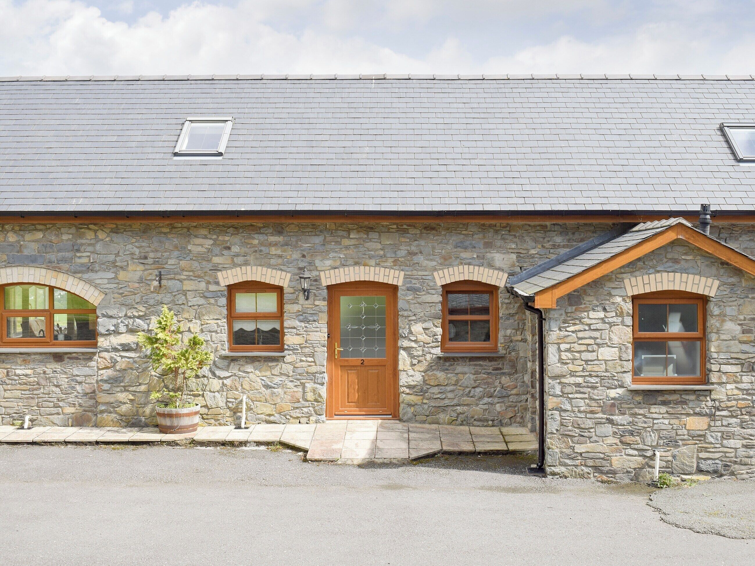 A stone building with a wooden door, three windows, and a small garden area.