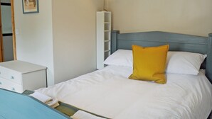 A neatly made bed with white and yellow pillows, a bedside table, and a small white cabinet. - 2 bedroom accommodation in Buxton (Buxton)