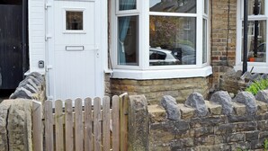 A corner of a house with a white door, a bay window, and a stone wall. - 2 bedroom accommodation in Buxton (Buxton)