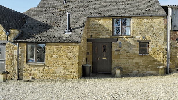 Un bâtiment en pierre avec une porte sombre, deux fenêtres et une cheminée.