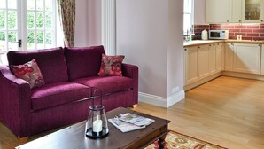 A living room with a purple sofa, a coffee table with a candle, and a kitchen area with cabinets and a microwave. - 1 bedroom accommodation in Moffat (Moffat)