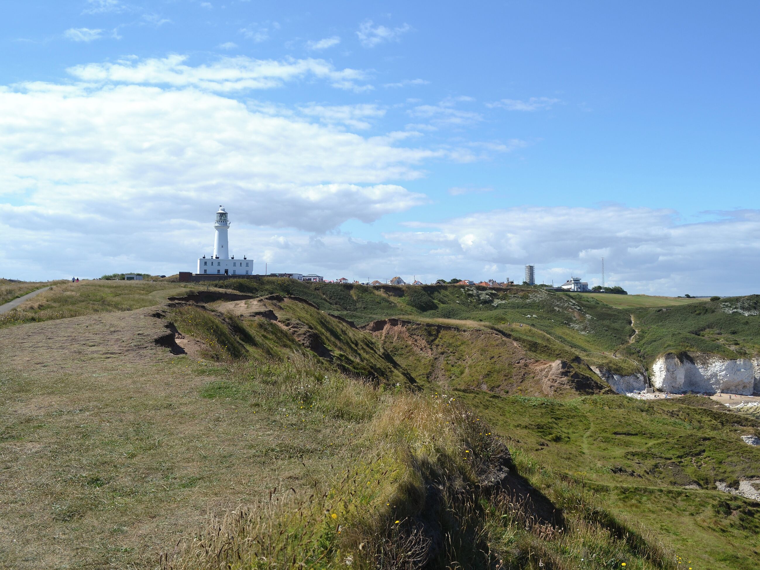 A lighthouse on a grassy hill with a clear sky.