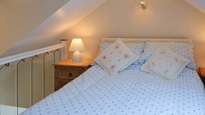 A bedroom with a bed, pillows, a nightstand, a lamp, and a wall-mounted light fixture.
