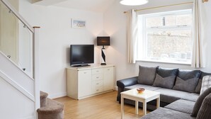 A living room with a sofa, a small table, a TV on a cabinet, a lamp, and a window with curtains.
