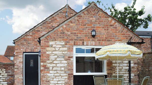 A brick building with a stone wall, a black door, a window, and a table with chairs.