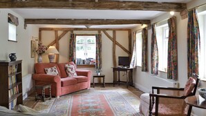 A cozy living room with a red sofa, a grey armchair, a wooden coffee table, and a patterned rug. - 2 bedroom accommodation in Aston Cantlow, near Stratford (Aston Cantlow, near Stratford)