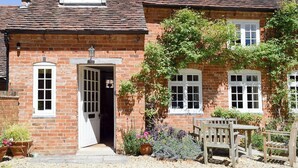 A traditional brick house with a gabled roof, a front door, and a small window above the door. There is a wooden bench and a potted plant in front of the house. - 2 bedroom accommodation in Aston Cantlow, near Stratford (Aston Cantlow, near Stratford)
