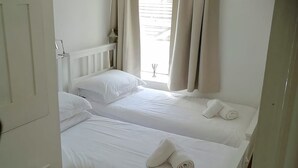 Ett hotellrum med två separata sängar, vitt sänglinne, ett fönster med gardiner och en vit garderob.