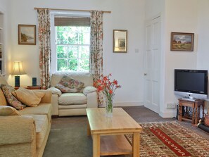 Ein Wohnzimmer mit einer Couch, einem Holztisch, einem Fernseher und einem Fenster mit Vorhängen.