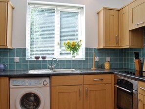 A kitchen with wooden cabinets, a built-in dishwasher, a stove, and a window with blinds.