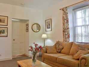 A living room with a beige sofa, a wooden coffee table, a vase with flowers, a lamp, and framed pictures on the wall.